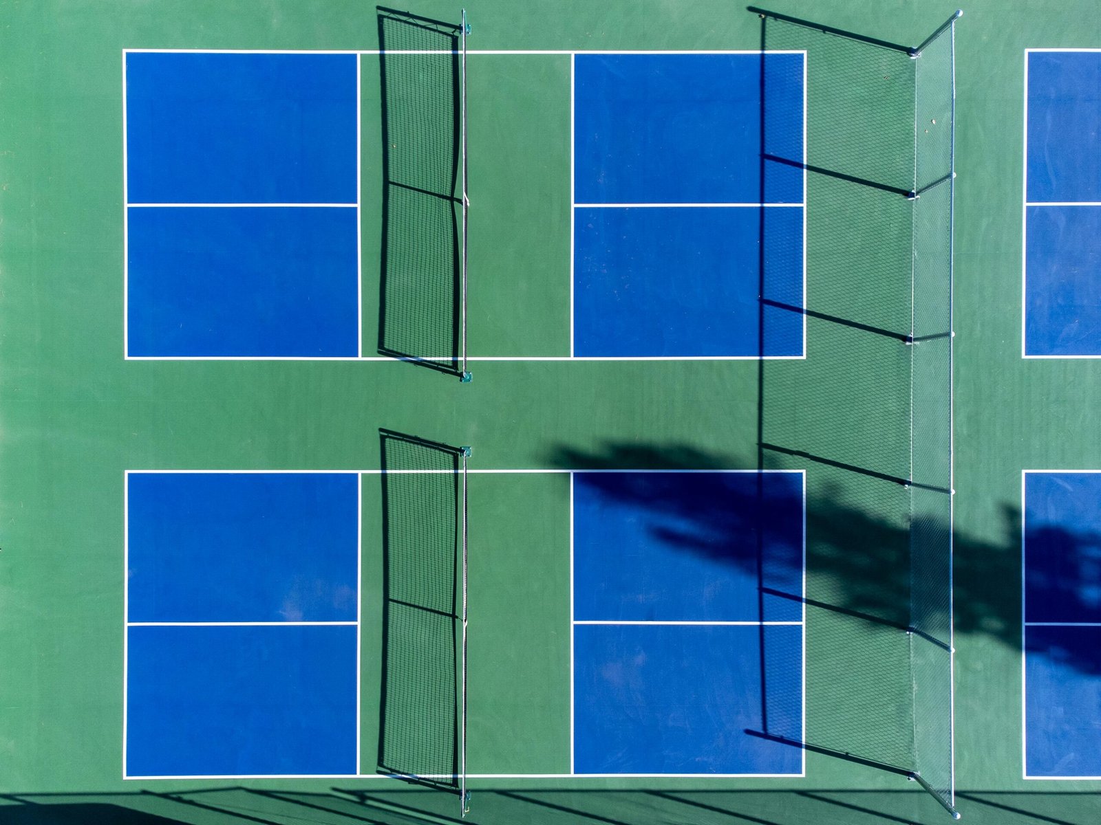 Top-down photo of vibrant blue and green sports courts with nets, perfect for recreational activities.