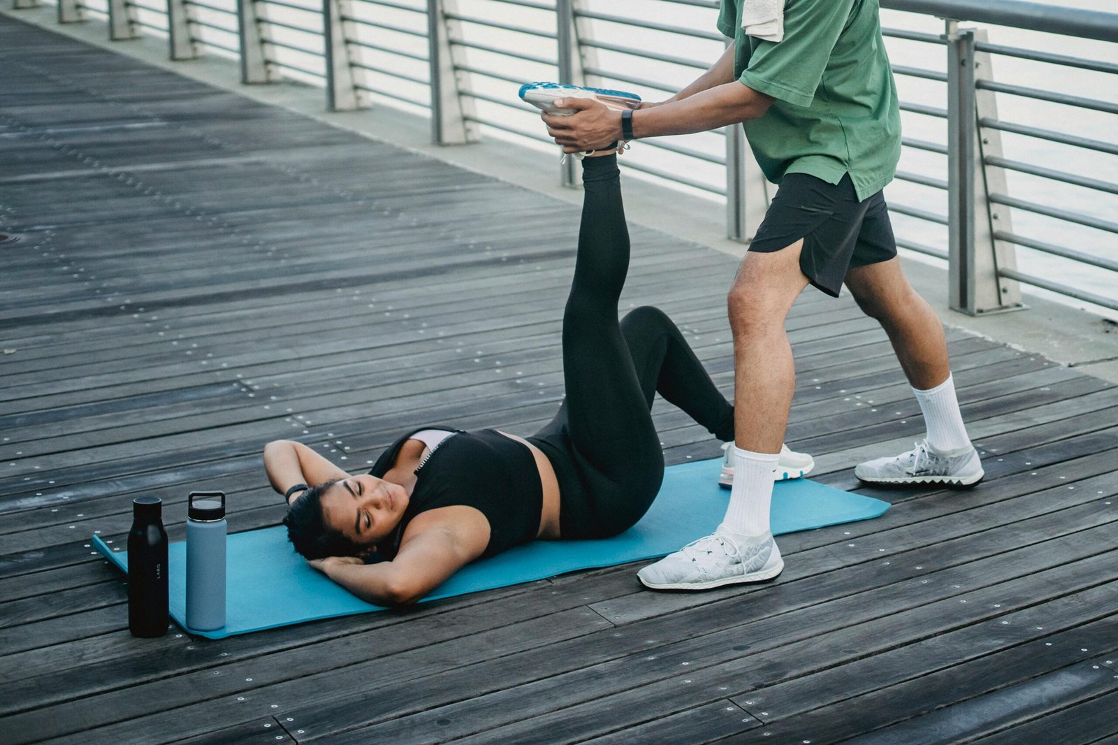 Woman stretching assisted by a trainer on a yoga mat outdoors.