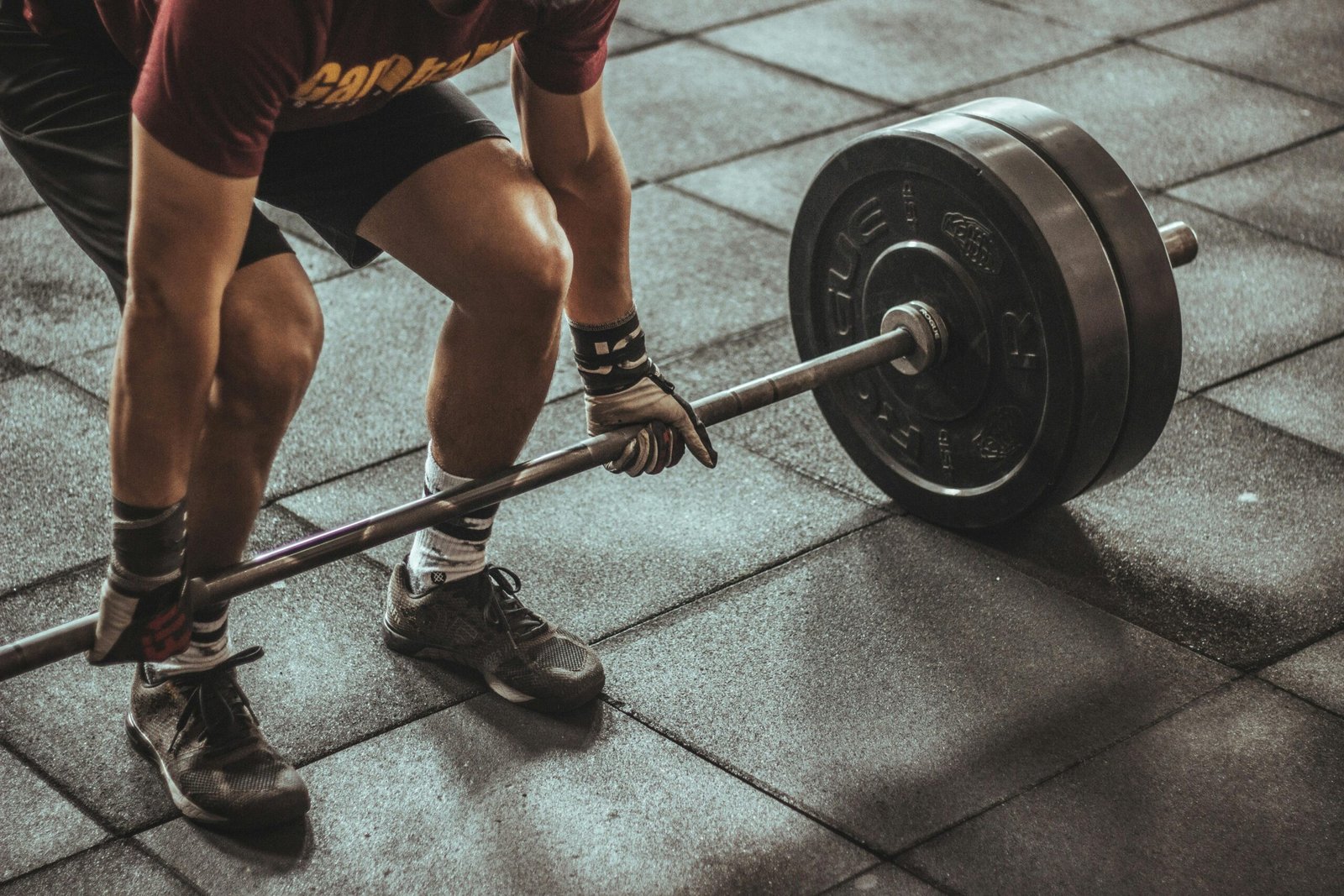 A focused weightlifter prepares to lift a heavy barbell in an indoor gym setting.